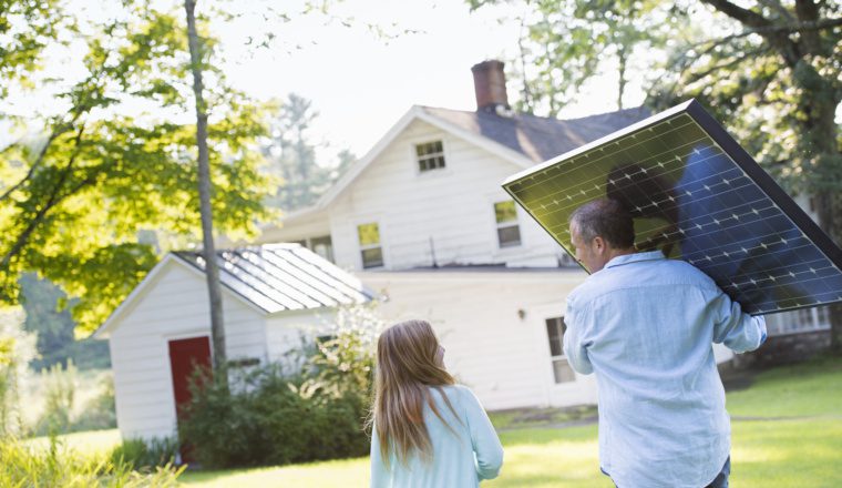 A man carrying a solar panel towards a building under construction.