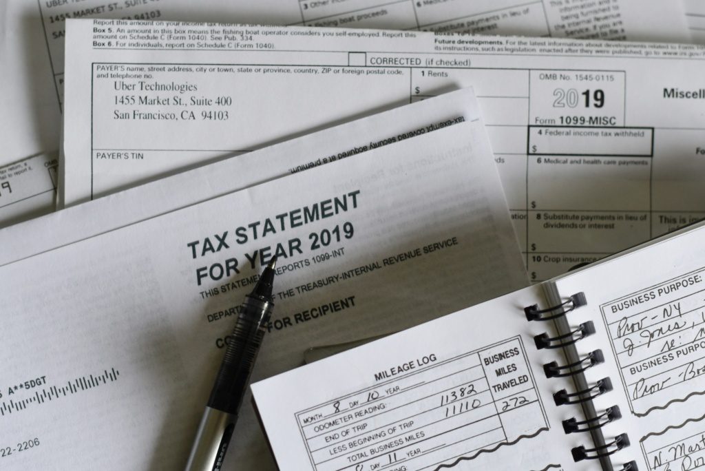 A collection of 2019 tax documents, a pen, and an open mileage logbook displaying handwritten entries photographed by Olga DeLawrence