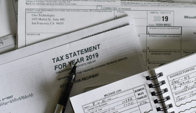 A collection of 2019 tax documents, a pen, and an open mileage logbook displaying handwritten entries photographed by Olga DeLawrence