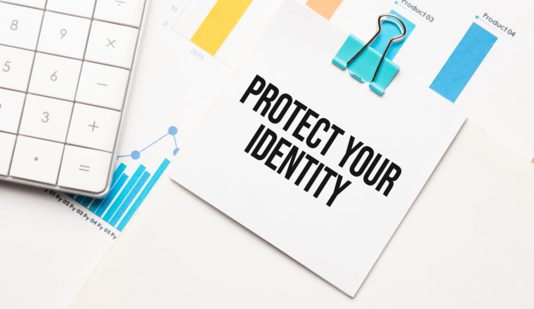 Protect Your Identity text on a notepad with a calculator and financial charts in the background.