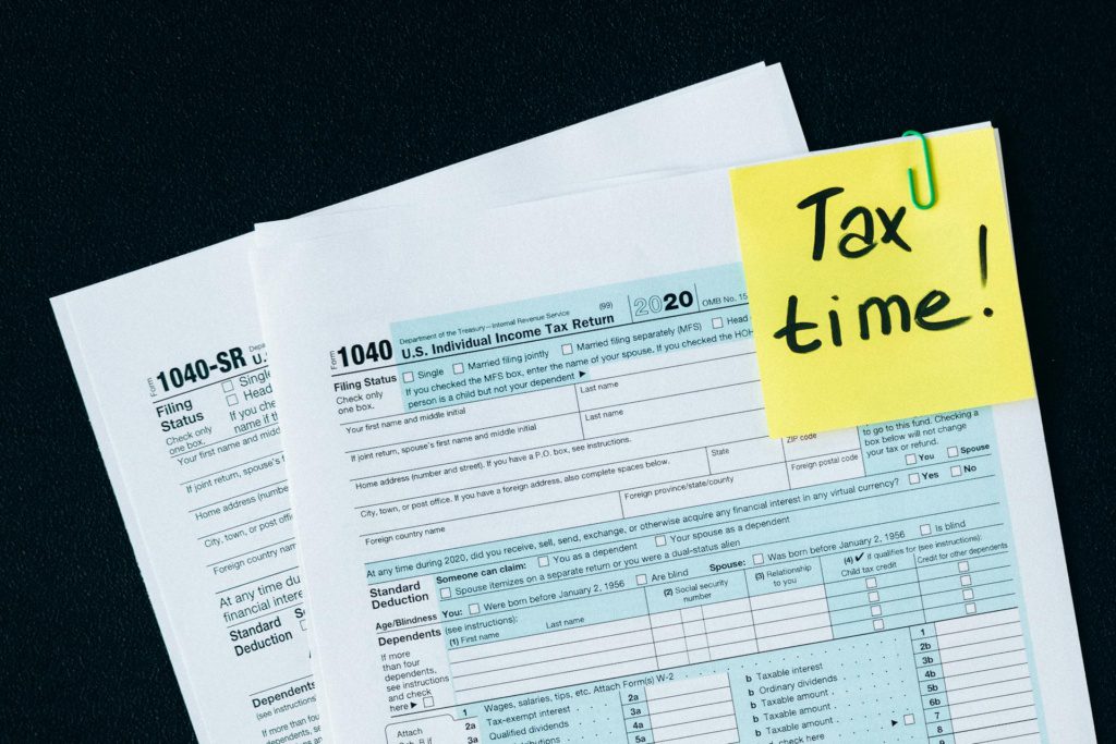 IRS tax forms with a sticky note reading 'Tax time!' clipped to the corner, symbolizing the urgency of tax filing deadlines.