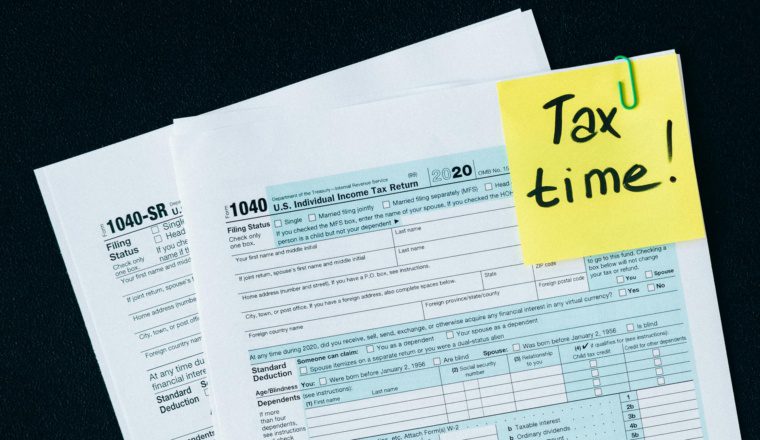 IRS tax forms with a sticky note reading 'Tax time!' clipped to the corner, symbolizing the urgency of tax filing deadlines.