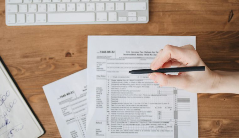 Person reviewing IRS tax forms and making notes at a desk, illustrating essentials for filing a 2024 tax return.