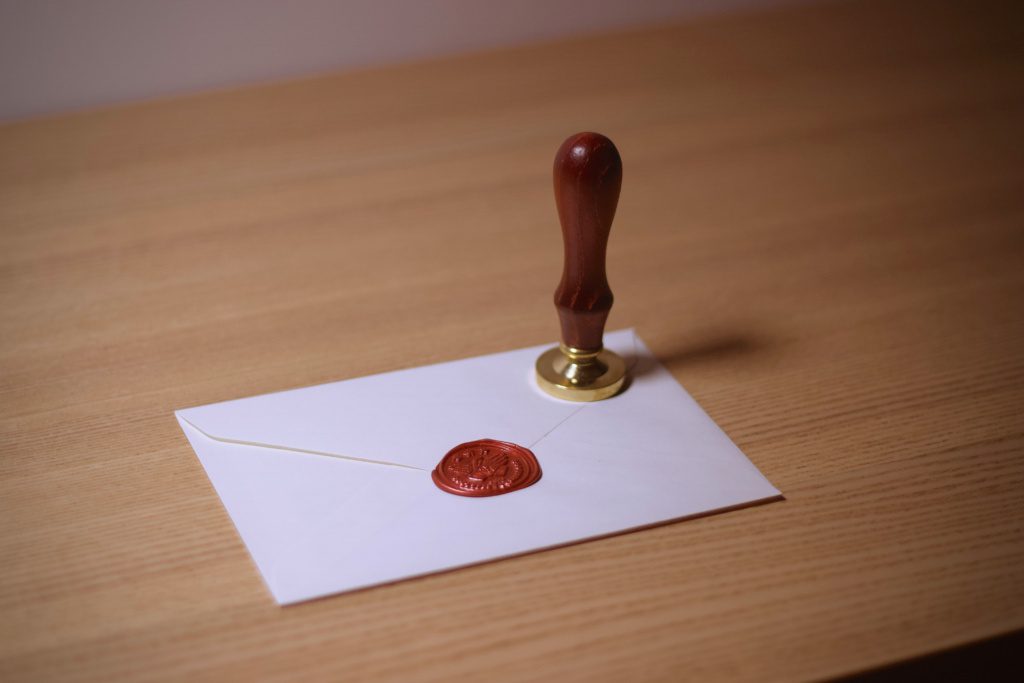 Featured image for how to know it’s the IRS: white envelope sealed with red wax and a brass stamp on a wooden desk.