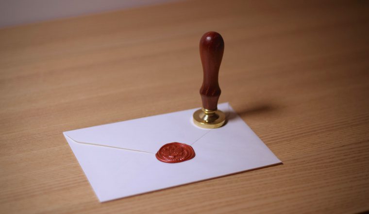 Featured image for how to know it’s the IRS: white envelope sealed with red wax and a brass stamp on a wooden desk.