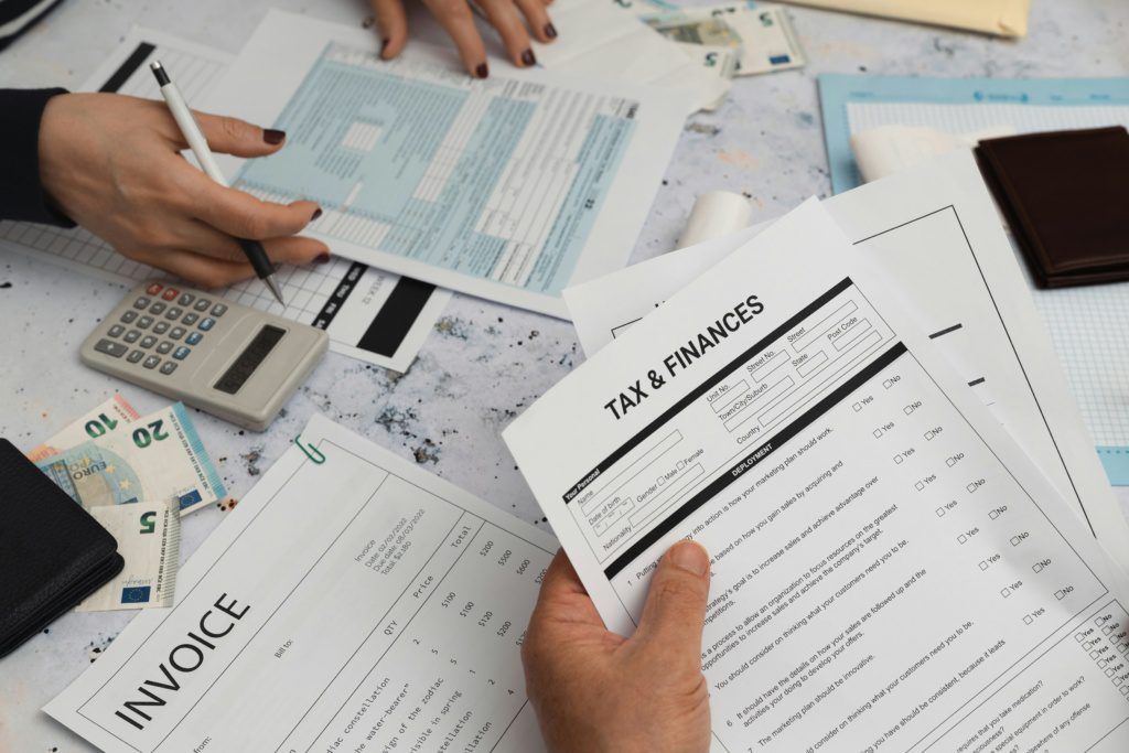 Hands reviewing tax and finances documents, invoices, and calculator on a desk, highlighting summer activities that impact your tax return.