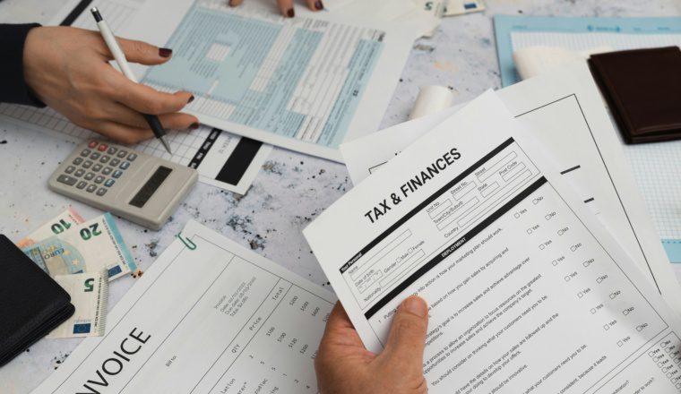 Hands reviewing tax and finances documents, invoices, and calculator on a desk, highlighting summer activities that impact your tax return.