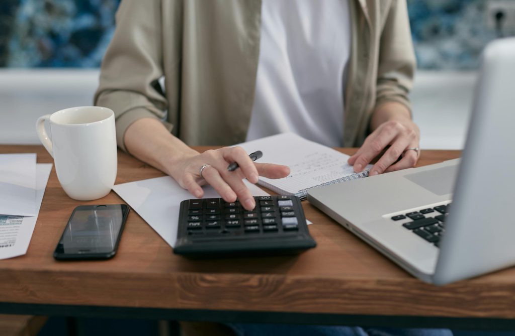Person using a calculator and laptop to plan retirement contributions under the 401(k) limit increases to $24,500 for 2026.