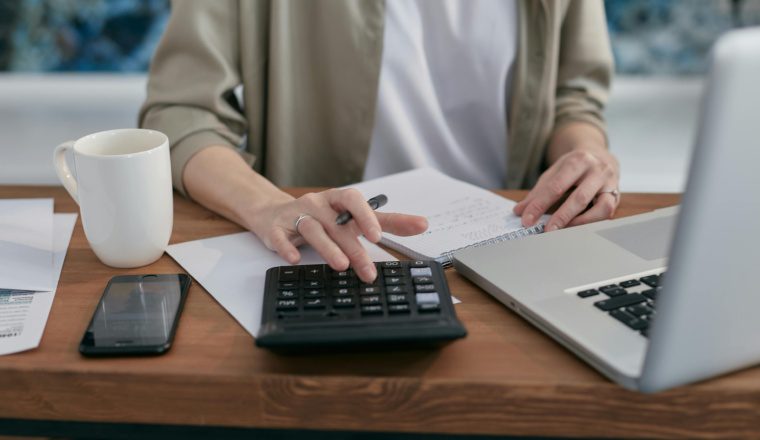 Person using a calculator and laptop to plan retirement contributions under the 401(k) limit increases to $24,500 for 2026.